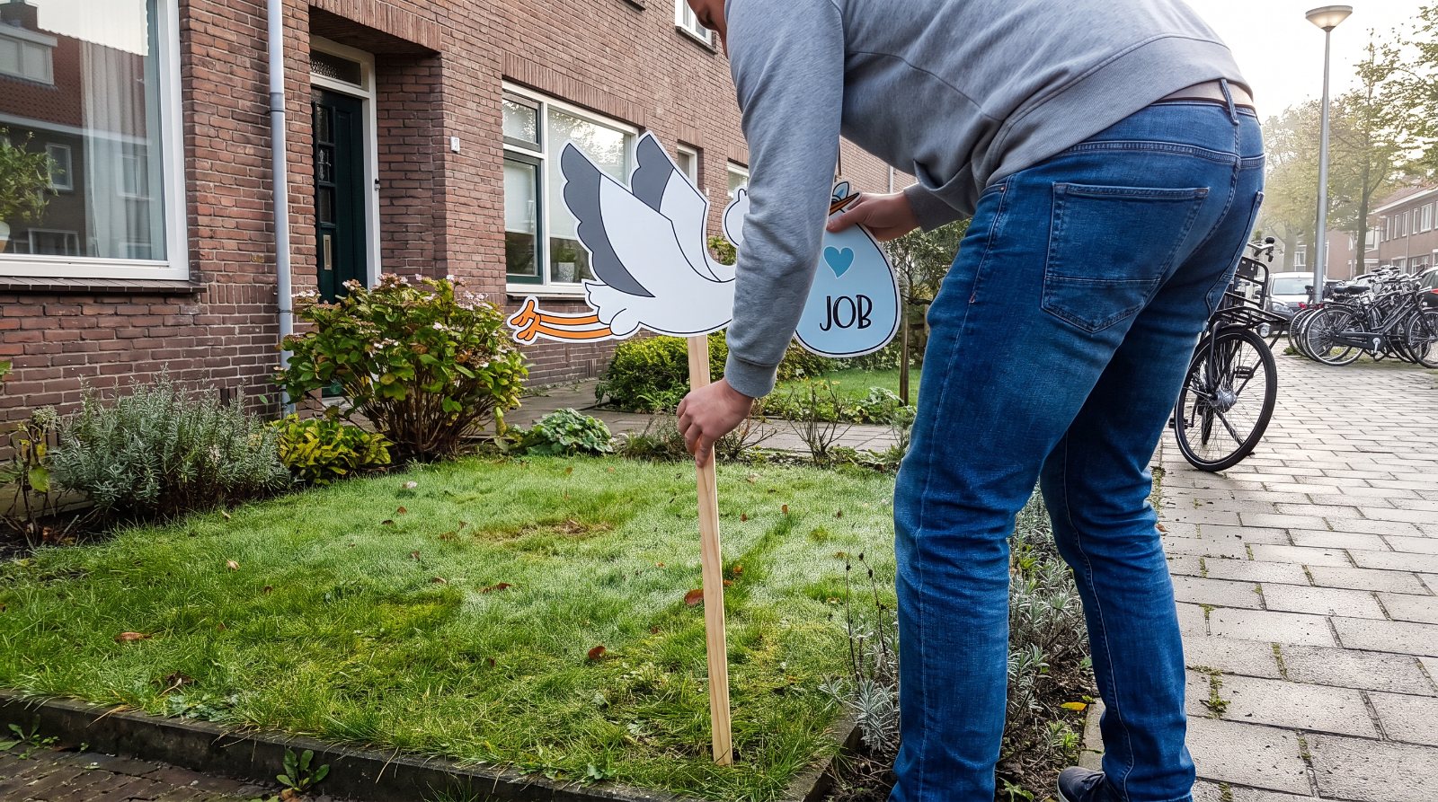 Vader zet een geboortebord met vliegende ooievaar in de voortuin